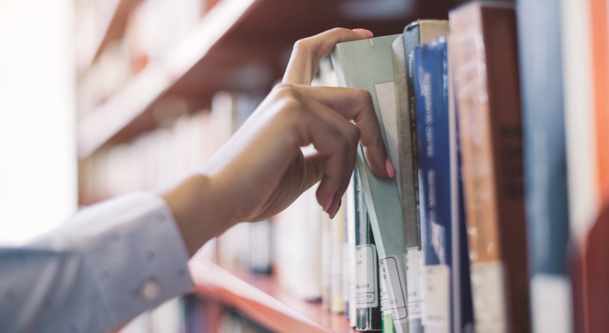 Picture of a person grabbing a book on a library shelf